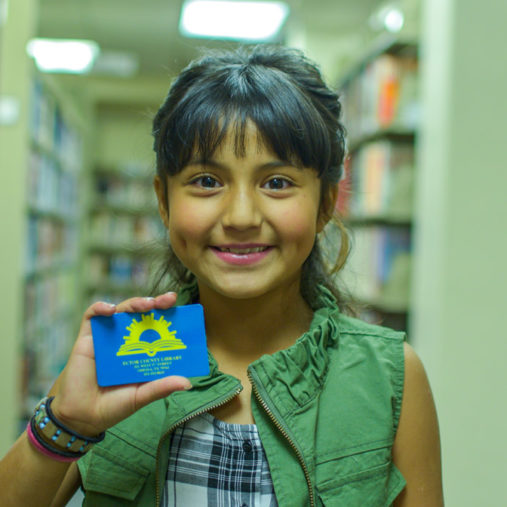 A young girl smiling and holding her library card